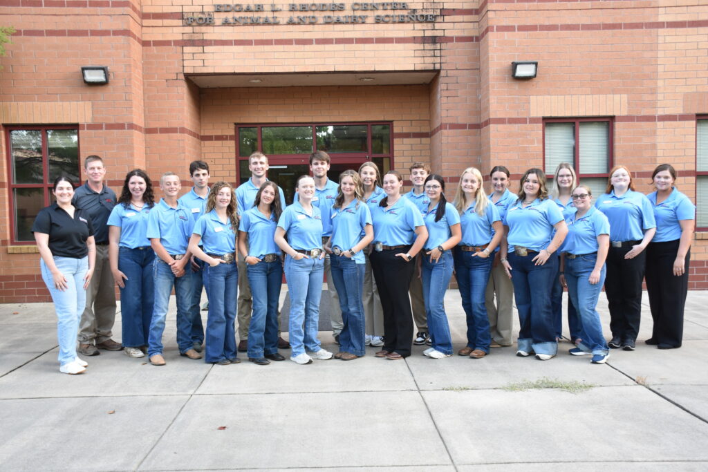 A group photo of 20 people standing outside in front of the entrance to the "Edgar L. Rhodes Center for Animal and Dairy Science" building.